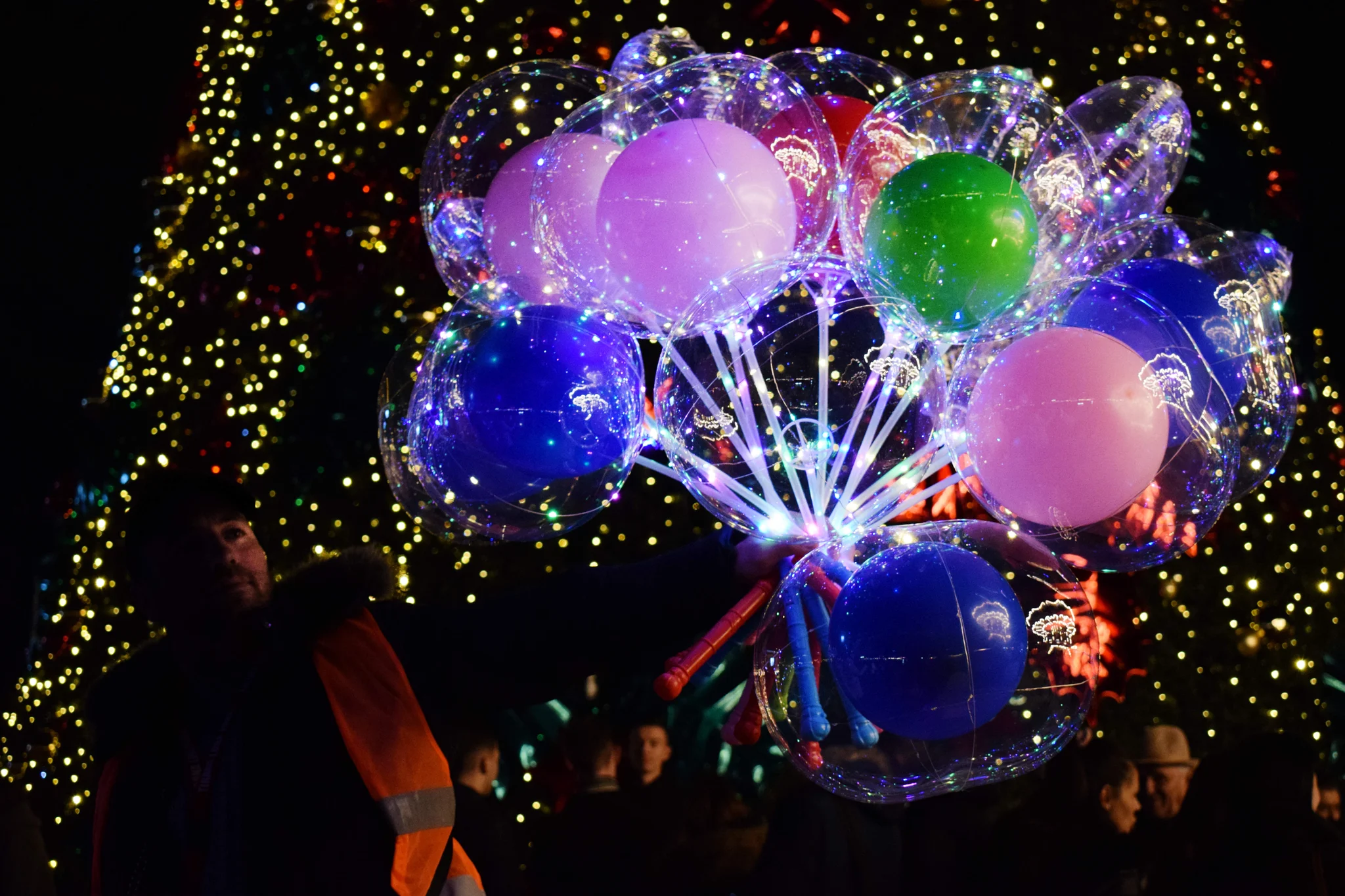 A man holding colourful balloons at night.